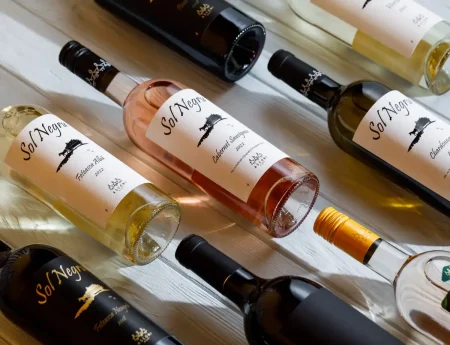 A collection of wine bottles from Asconi Winery displayed on a white wooden table. The bottles feature labels with the name "Sol Negru" and different grape varieties like Feteasca Alba, Cabernet Sauvignon, and Chardonnay