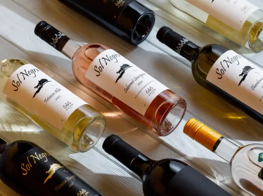 A collection of wine bottles from Asconi Winery displayed on a white wooden table. The bottles feature labels with the name "Sol Negru" and different grape varieties like Feteasca Alba, Cabernet Sauvignon, and Chardonnay